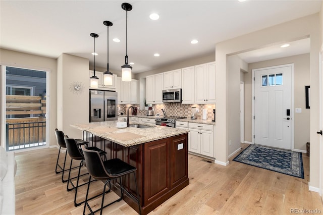8186 E 53rd Dr, Denver, CO 80238 - kitchen featuring appliances with stainless steel finishes, backsplash, light wood-type flooring, white cabinets, and a center island with sink