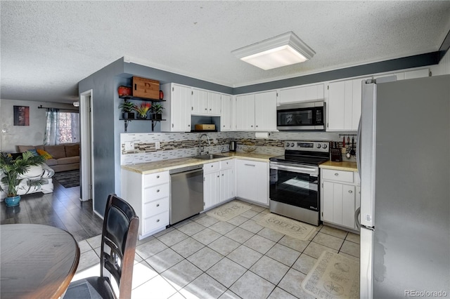 kitchen featuring sink, a textured ceiling, appliances with stainless steel finishes, light tile patterned flooring, and white cabinetry