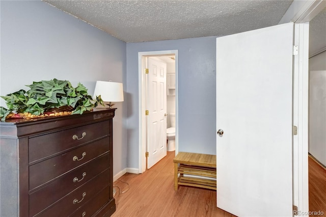 bedroom featuring ensuite bathroom, light hardwood / wood-style flooring, and a textured ceiling