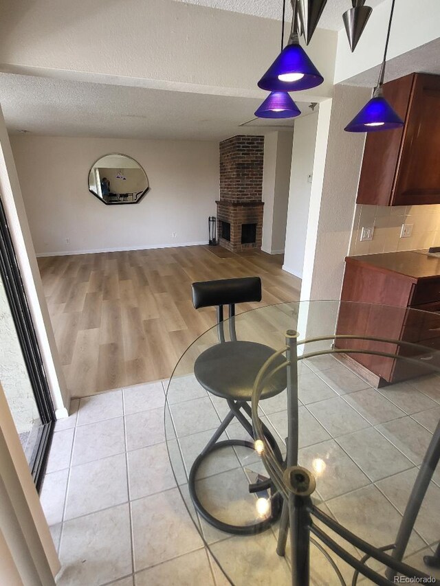 living area featuring baseboards, a textured ceiling, a brick fireplace, and light tile patterned flooring