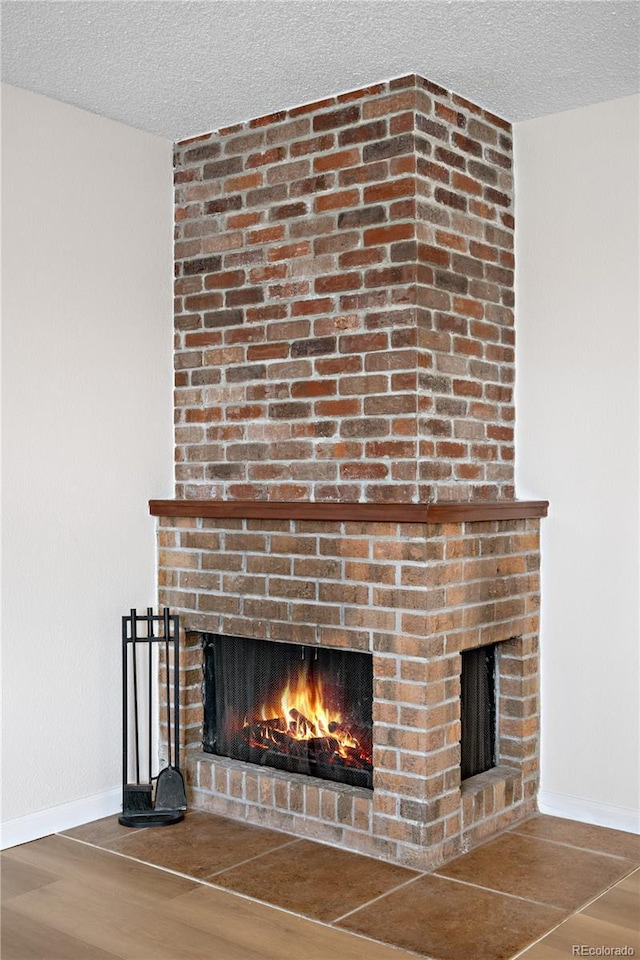 room details with baseboards, a brick fireplace, a textured ceiling, and wood finished floors