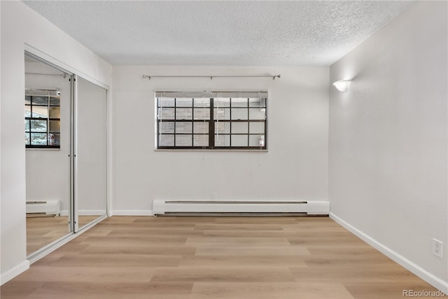 unfurnished bedroom with a textured ceiling, baseboard heating, and wood finished floors