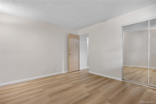 unfurnished bedroom with baseboards, a textured ceiling, wood finished floors, and a closet