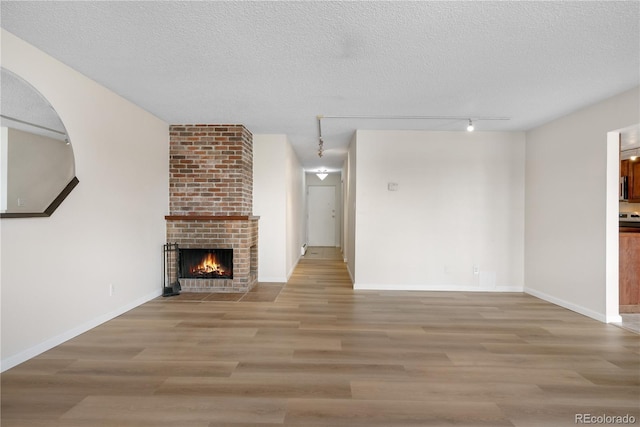 unfurnished living room with rail lighting, a textured ceiling, wood finished floors, and a fireplace