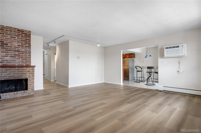 unfurnished living room featuring track lighting, an AC wall unit, light wood-type flooring, and a textured ceiling
