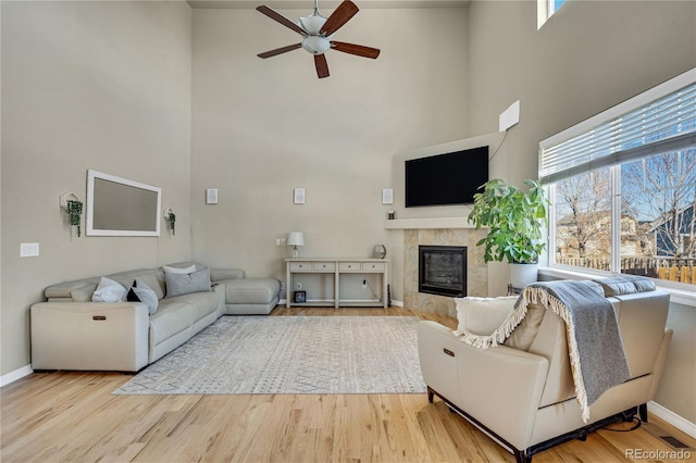 living room with a high ceiling, a tile fireplace, ceiling fan, and light wood-type flooring