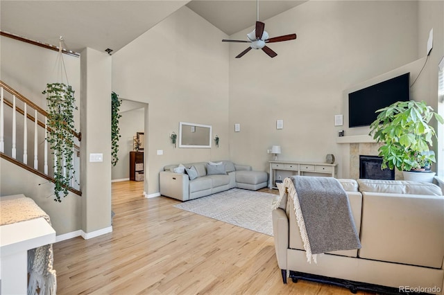 living room with a tile fireplace, a towering ceiling, ceiling fan, and light hardwood / wood-style flooring