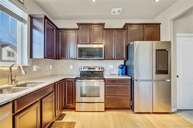 kitchen with sink, backsplash, light stone counters, light hardwood / wood-style floors, and stainless steel appliances