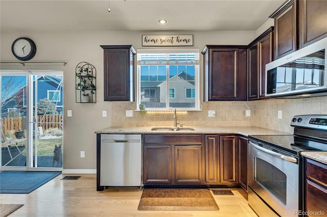 kitchen with sink, light stone counters, light hardwood / wood-style flooring, stainless steel appliances, and backsplash