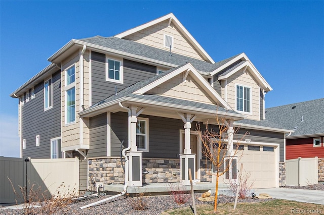 view of front facade featuring a garage, stone siding, covered porch, and fence