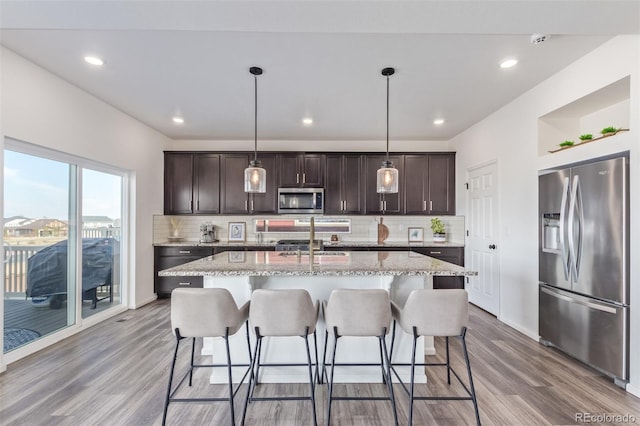 kitchen featuring dark brown cabinets, a breakfast bar area, appliances with stainless steel finishes, light wood-style floors, and a sink