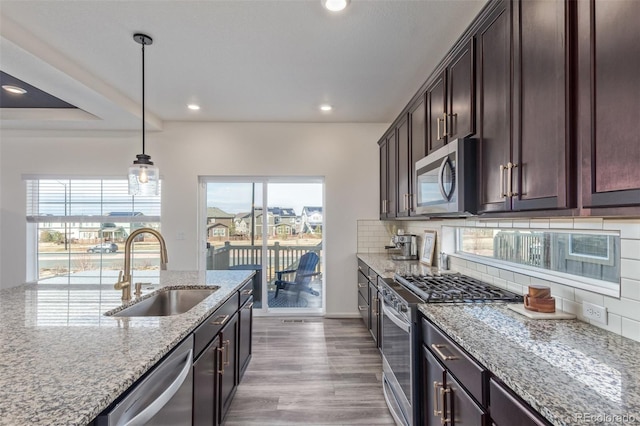 kitchen featuring a sink, tasteful backsplash, stainless steel appliances, dark brown cabinetry, and light stone countertops