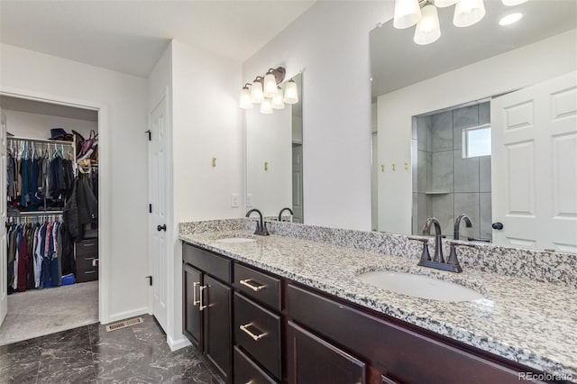 bathroom featuring double vanity, marble finish floor, a walk in closet, and a sink