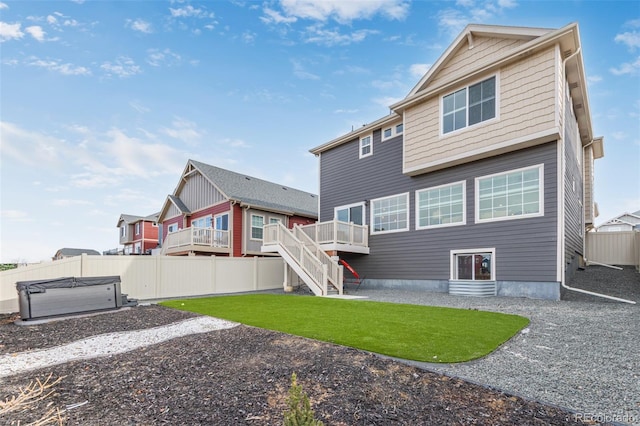 rear view of property featuring a hot tub, fence, stairs, a deck, and a yard