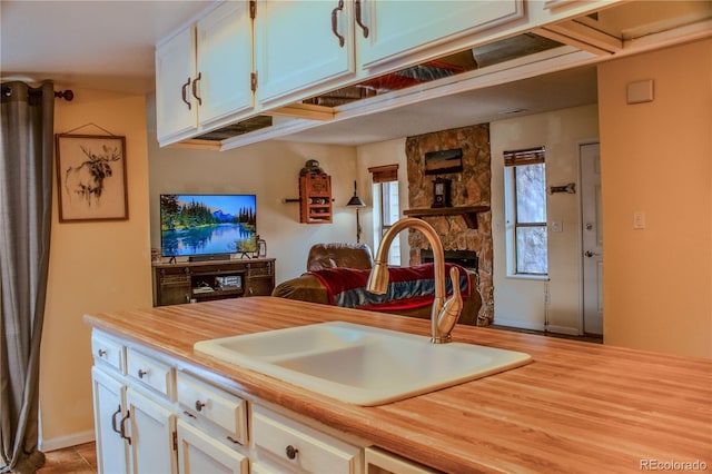 kitchen with a sink, wood counters, open floor plan, white cabinets, and a fireplace