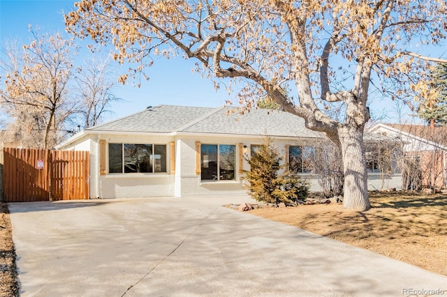 rear view of house with brick siding, a shingled roof, and fence