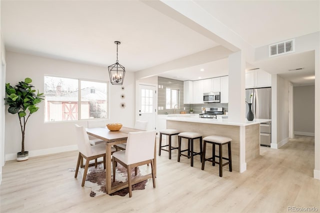 dining space with an inviting chandelier, light wood-type flooring, visible vents, and baseboards