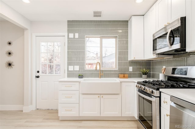 kitchen featuring stainless steel appliances, light countertops, a sink, and white cabinetry