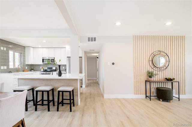 kitchen with light wood finished floors, visible vents, stainless steel appliances, a kitchen bar, and backsplash