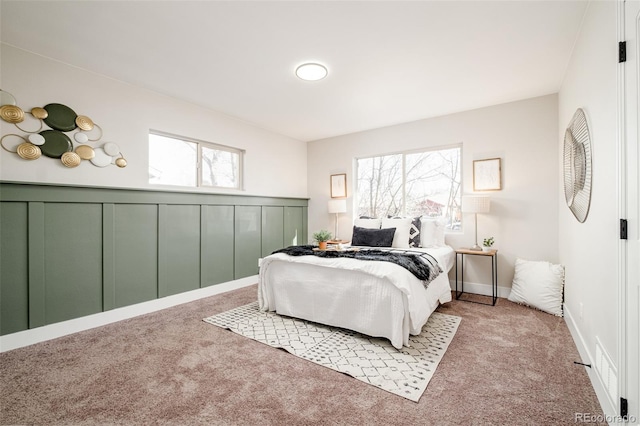 carpeted bedroom with a wainscoted wall and a decorative wall