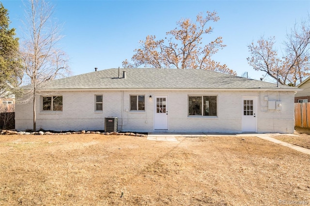 back of house featuring brick siding, roof with shingles, cooling unit, and fence