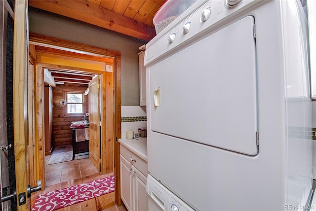 clothes washing area with cabinets, stacked washer and dryer, wood ceiling, and log walls