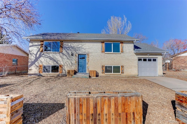 bi-level home with brick siding, concrete driveway, an attached garage, entry steps, and fence