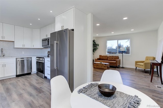 kitchen featuring a sink, decorative backsplash, stainless steel appliances, white cabinetry, and light wood-type flooring