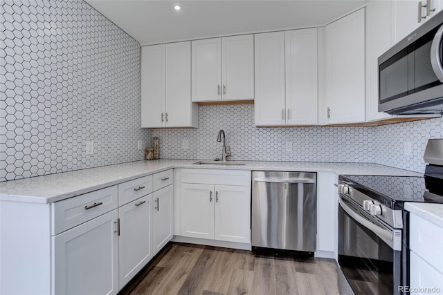 kitchen featuring dark wood finished floors, a sink, appliances with stainless steel finishes, white cabinetry, and backsplash