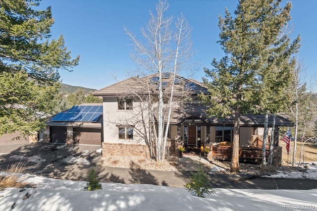 view of front facade featuring a garage, roof mounted solar panels, a wooden deck, and stucco siding