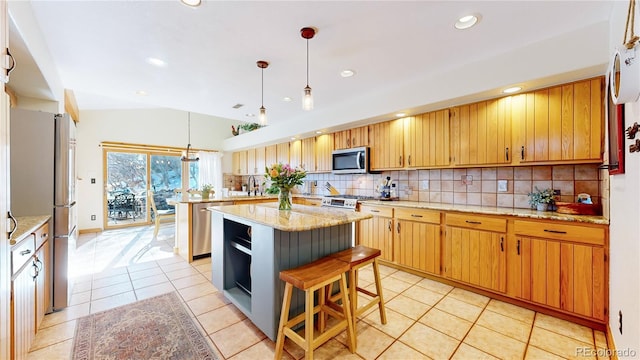 kitchen with light tile patterned floors, appliances with stainless steel finishes, decorative light fixtures, a kitchen breakfast bar, and a kitchen island