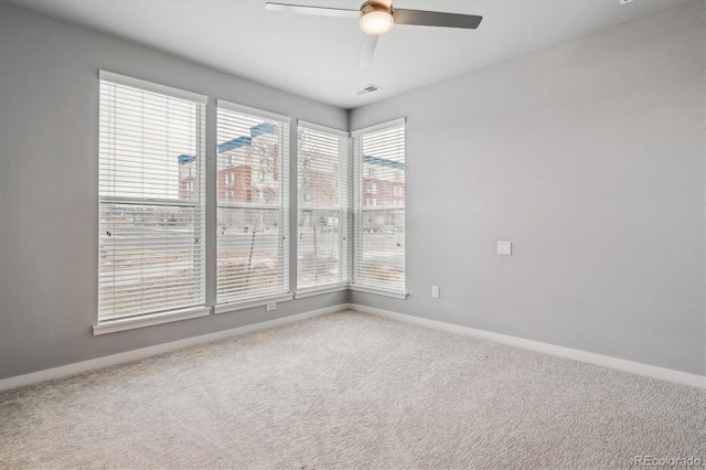 carpeted empty room with ceiling fan, visible vents, and baseboards