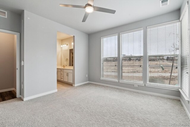 unfurnished bedroom with light colored carpet, visible vents, ensuite bathroom, a ceiling fan, and baseboards