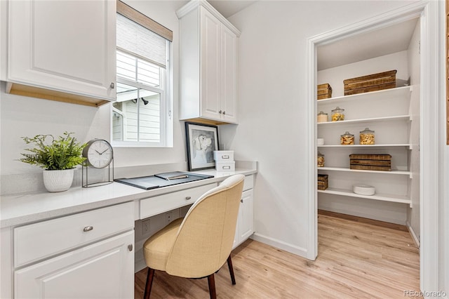 office space featuring light wood finished floors, baseboards, and built in desk