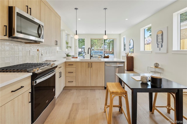 kitchen with pendant lighting, light brown cabinets, sink, light hardwood / wood-style flooring, and appliances with stainless steel finishes