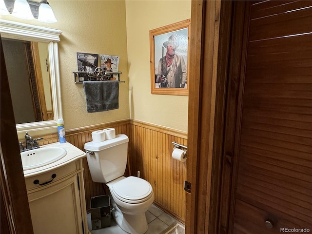 bathroom featuring toilet, vanity, wood walls, and tile patterned flooring