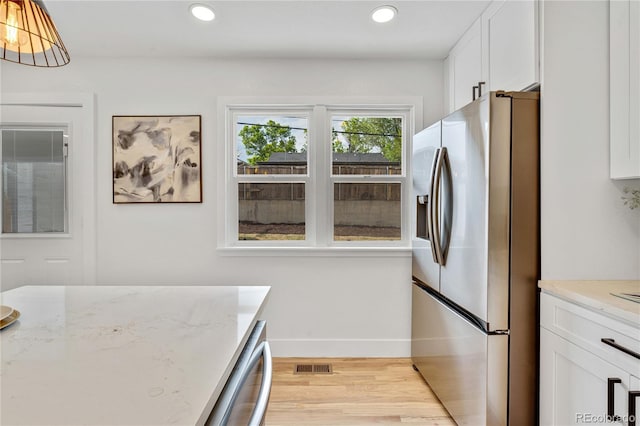 2701 Barnhart St, Thornton, CO 80229 - kitchen with stainless steel fridge, white cabinetry, light wood-type flooring, baseboards, and light stone counters