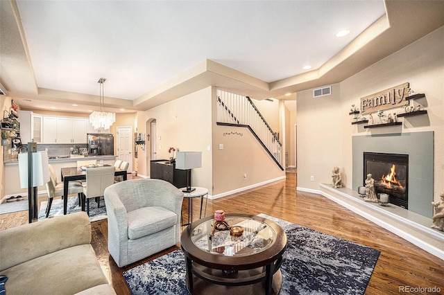 12051 E Lake Cir, Greenwood Village, CO 80111 - living room featuring a raised ceiling, a tiled fireplace, light wood-style flooring, stairs, and a chandelier