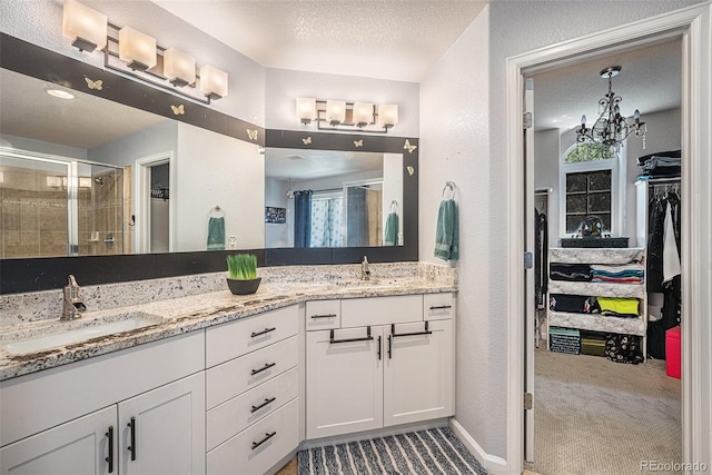 12051 E Lake Cir, Greenwood Village, CO 80111 - bathroom with double vanity, a stall shower, a spacious closet, a textured wall, and a chandelier