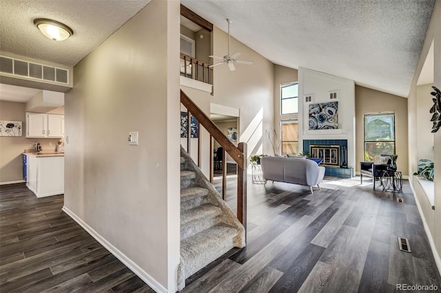 staircase with a fireplace, hardwood / wood-style flooring, high vaulted ceiling, and ceiling fan