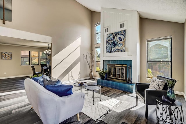 living room with high vaulted ceiling, hardwood / wood-style flooring, a tiled fireplace, and a notable chandelier