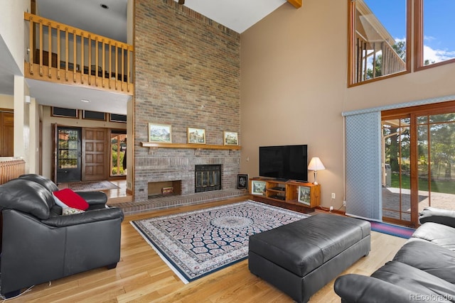 living room with a high ceiling, a brick fireplace, and light hardwood / wood-style flooring