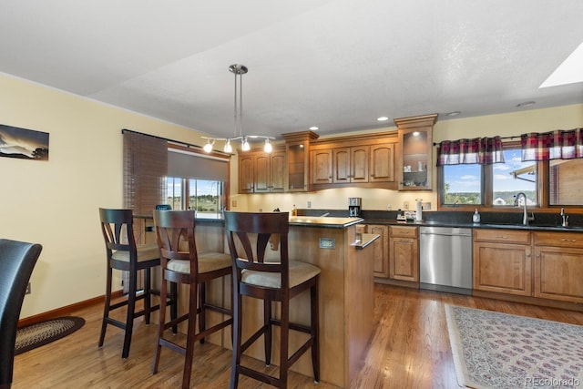 kitchen with sink, a breakfast bar area, a kitchen island, decorative light fixtures, and stainless steel dishwasher