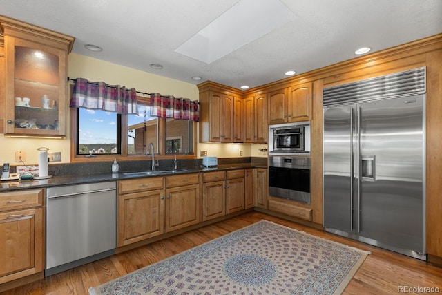 kitchen featuring a skylight, appliances with stainless steel finishes, sink, and light hardwood / wood-style flooring