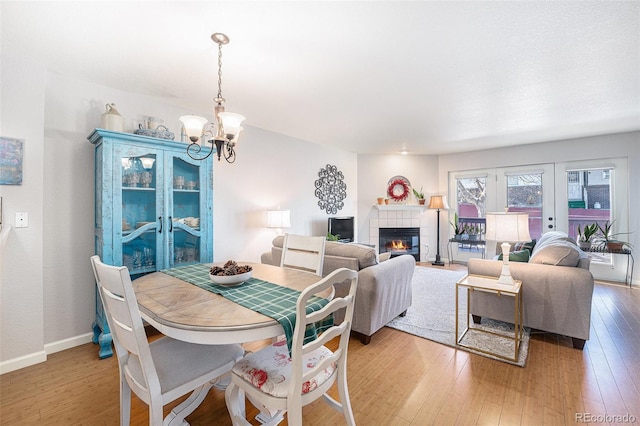 5252 W 68th Ave, Arvada, CO 80003 - dining space featuring a chandelier, light wood-type flooring, a tiled fireplace, and baseboards