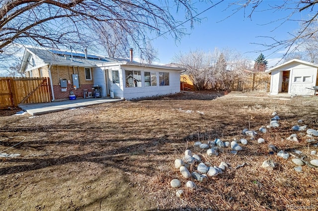 rear view of property featuring a storage shed, solar panels, an outbuilding, fence, and brick siding