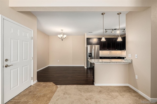 kitchen with light stone counters, hanging light fixtures, stainless steel fridge, and kitchen peninsula