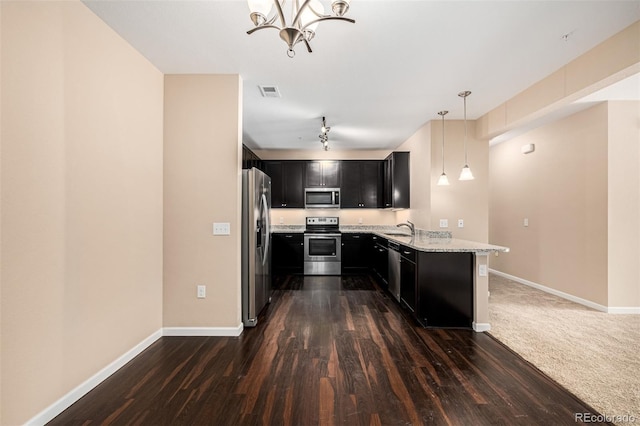 kitchen with pendant lighting, kitchen peninsula, sink, appliances with stainless steel finishes, and light stone counters