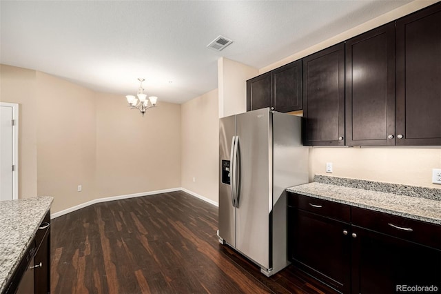 kitchen with stainless steel refrigerator with ice dispenser, light stone countertops, dark brown cabinets, and a notable chandelier