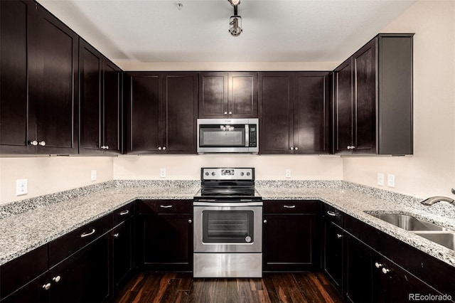 kitchen with appliances with stainless steel finishes, dark wood-type flooring, dark brown cabinets, light stone counters, and sink